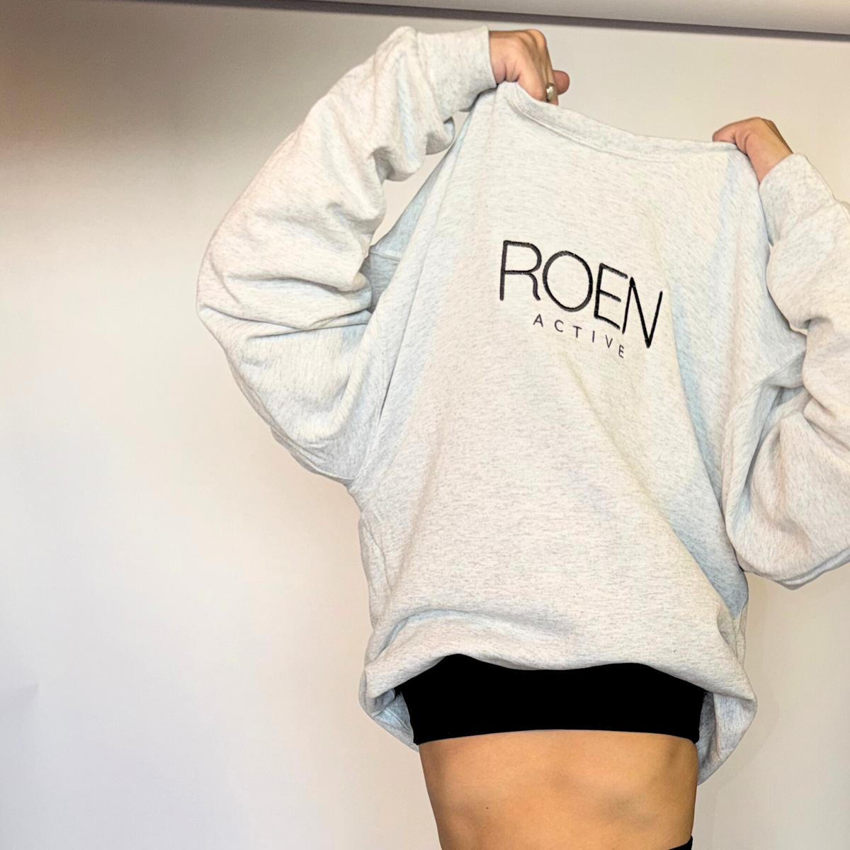 Gray sweatshirt with 'ROEN ACTIVE' logo held by a person against a plain background