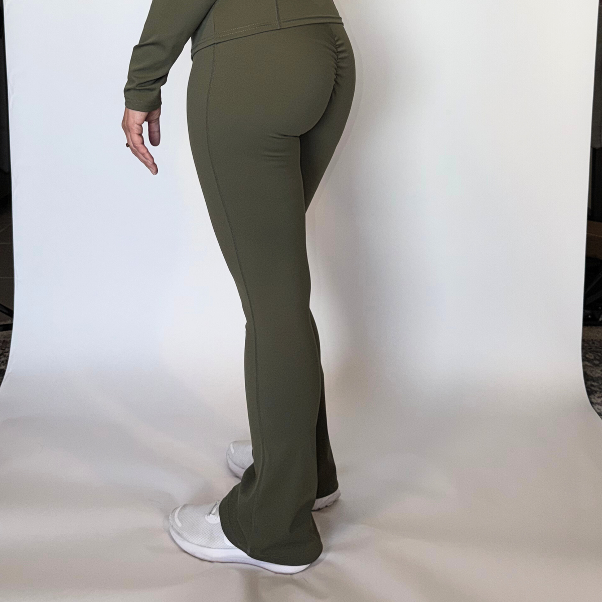 Person wearing olive green pants and white shoes on a plain background